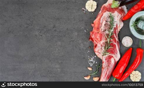 Raw whole leg of lamb, shoulder of lamb, with spices, condiments and herbs in the concept of cooking dish. Top view, fresh meat on a dark stone table, product layout with copy space for recipe