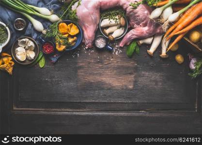 Raw whole rabbit with fresh vegetables and mushrooms for tasty rabbit stew cooking. Preparation of hunting stew on dark aged rustic background, top view border