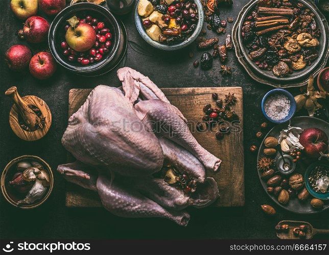 Raw whole turkey stuffed with dried fruits and apples on wooden cutting board, dark kitchen table background with ingredients , top view. Cooking preparation for Thanksgiving or Christmas dinner.