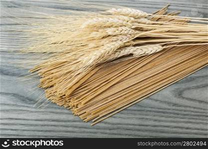 Raw whole wheat spaghetti with wheat kernels on top with white ash wood in background