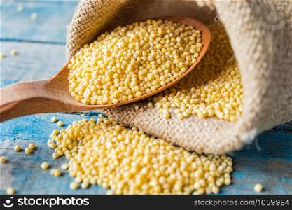 Raw yellow millet in a wooden spoon on burlap cloth on a background of blue rustic boards. Close-up.. Raw yellow millet in a wooden spoon on burlap cloth on a background of blue rustic boards.