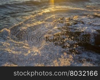 Ray of Light hitting seaspray as a wave crashes onto dark limestone. Mediterranean coast, Mallorca, Balearic islands, Spain.