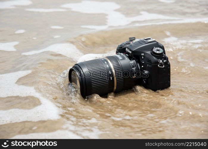 Rayong, Thailand - May 27, 2017 : Unidentified photographer demo waterproof DSLR camera with telephoto lens on beach it wet from water sea wave when travel and test using in the extreme environment. DSLR camera on beach wet from water sea wave