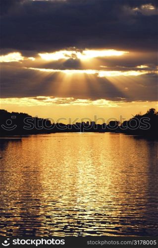 Rays of sun shining through the clouds and sunset over water