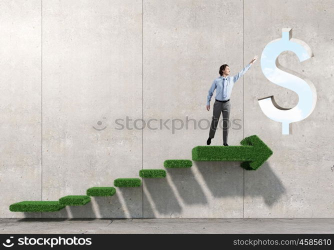 Reaching financial success. Businessman standing on graph and reaching hand to touch dollar sign