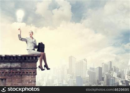 Reaching the top. Fearless businesswoman with suitcase sitting on building top