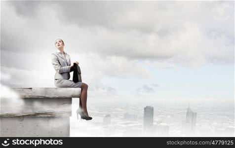 Reaching the top. Fearless businesswoman with suitcase sitting on building top