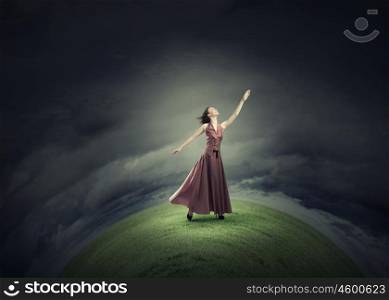 Reaching the top. Young woman in evening dress standing on green hill