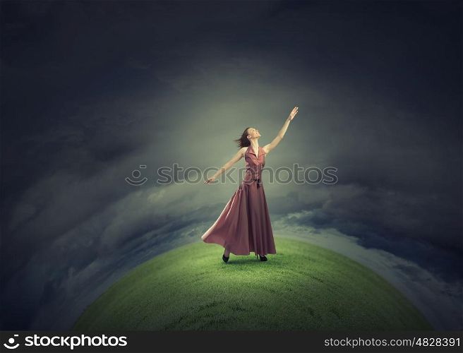 Reaching the top. Young woman in evening dress standing on green hill