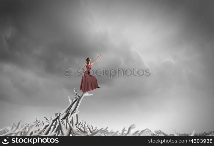 Reaching the top. Young woman in evening dress walking on hands of crowd of people