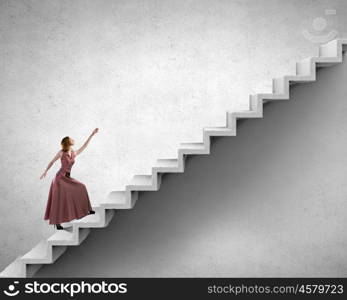 Reaching the top. Young woman in evening long dress walking up the staircase