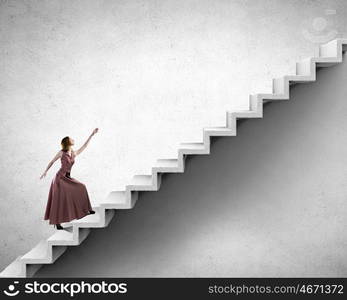 Reaching the top. Young woman in evening long dress walking up the staircase