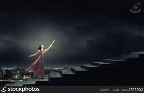 Reaching the top. Young woman in evening long dress walking up the staircase