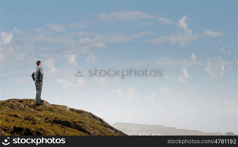 Reaching top of success. Rear view of confident businessman standing on rock top