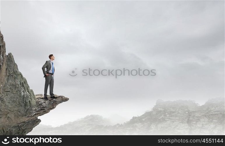 Reaching top of success. Young confident businessman standing on rock top