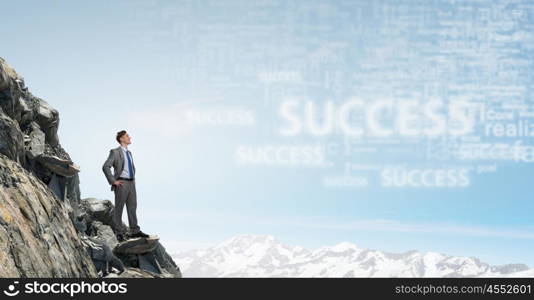 Reaching top of success. Young confident businessman standing on rock top