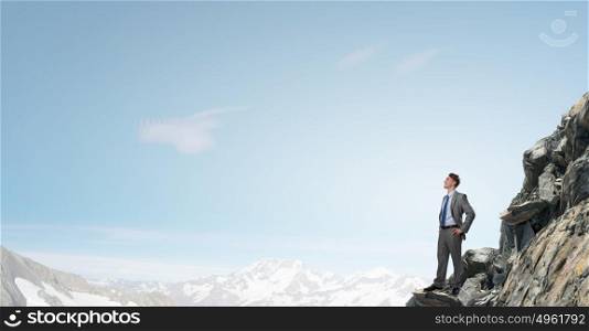 Reaching top of success. Young confident businessman standing on rock top