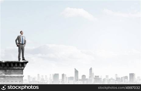 Reaching top of success. Young confident businessman standing on top of building