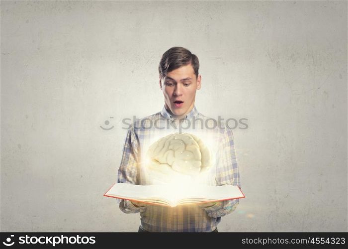 Read and broaden your mind. Shocked man holding opened book with brain picture
