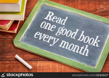 Read one good book every month - advice or reminder on a slate blackboard with a white chalk and a stack of books against rustic wooden table