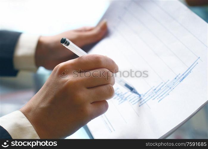read the graph in financial report, hand pointing at graph with pen. read financial report