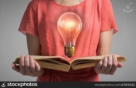 Read to broaden your mind. Close view of woman holding book with light bulb on pages