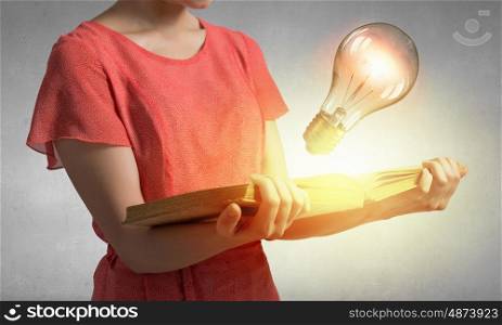 Read to broaden your mind. Close view of woman holding book with light bulb on pages