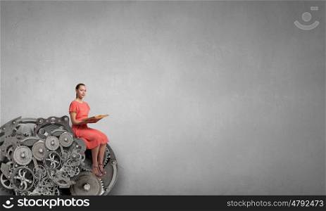 Read to broaden your mind. Young attractive woman sitting on gear mechanism and reading book
