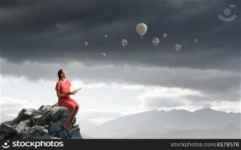 Read to broaden your mind. Young attractive woman sitting on rock edge and reading book