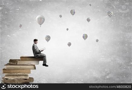 Read to broaden your mind. Young businessman sitting in pile of old books