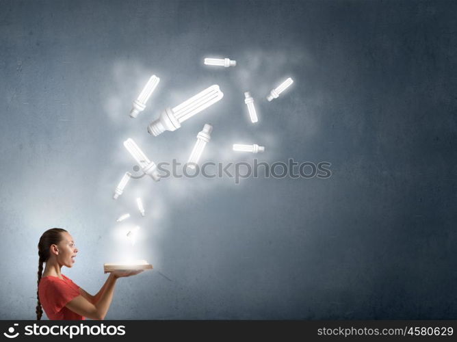 Read to broaden your mind. Young woman holding book with light bulb on pages