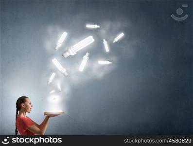 Read to broaden your mind. Young woman holding book with light bulb on pages