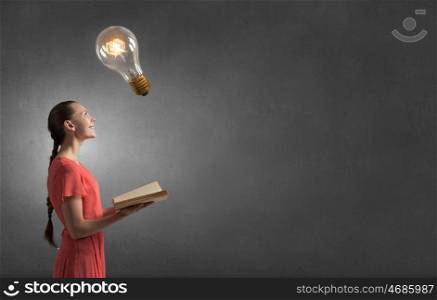 Read to broaden your mind. Young woman holding book with light bulb on pages