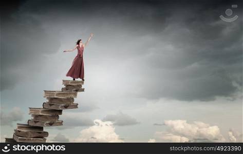 Reading and education. Woman in long dress with blindfold on eyes standing on pile of books