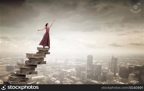 Reading and education. Woman in long dress with blindfold on eyes standing on pile of books