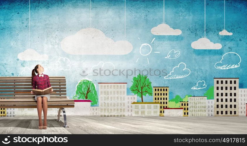 Reading and imagination. Young woman sitting on bench and reading book