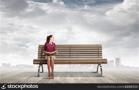 Reading and imagination. Young woman sitting on bench and reading book