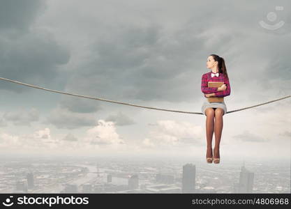 Reading and imagination. Young woman sitting on rope above city and reading book