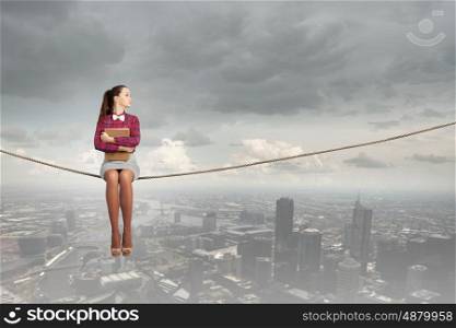 Reading and imagination. Young woman sitting on rope above city and reading book