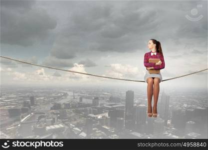 Reading and imagination. Young woman sitting on rope above city and reading book