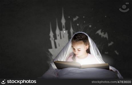Reading before sleep. Cute girl in bed under blanket with book in hands
