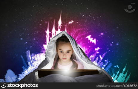 Reading before sleep. Cute girl in bed under blanket with book in hands