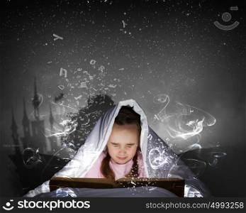 Reading before sleep. Cute girl in bed under blanket with book in hands