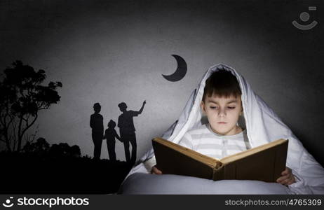 Reading before sleep. Little cute boy reading book in bed under blanket