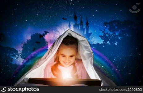 Reading before sleep. Little cute girl with in bed reading book under blanket