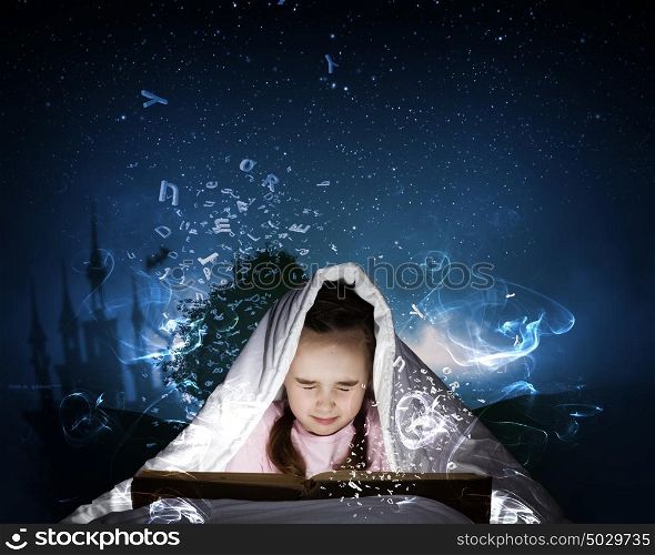 Reading before sleep. Little cute girl with in bed reading book under blanket