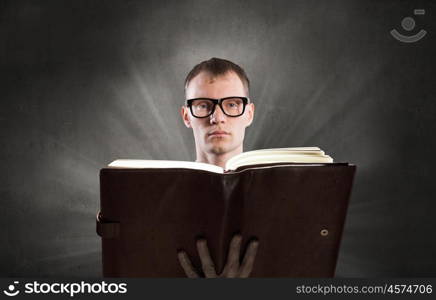 Reading book. Young man in glasses with opened book in hands