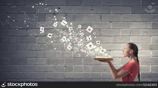 Reading books. Young girl with book in hands blowing letters from pages