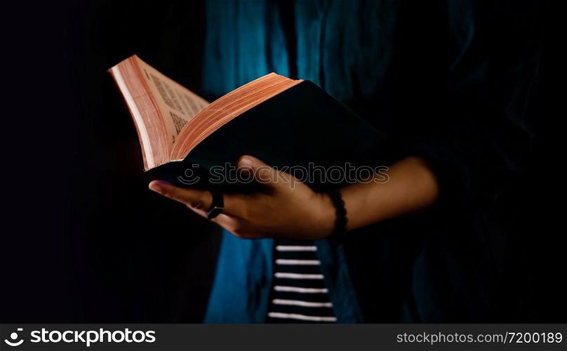 Reading Concept. Person Holding Opened Bible Book on Hand. Dark Tone, Cropped image