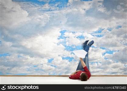 Reading develope imagination. Young man lying on floor with legs raised up